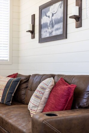 Ein braunes Ledersofa mit gemusterten Kissen, ein gerahmtes Bild an der Wand und eine wandmontierte Leuchte.