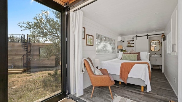 Un dormitorio con cama, una silla, una ventana y vistas al exterior.