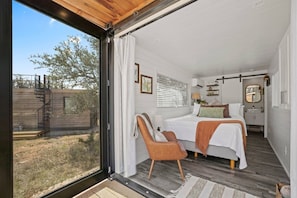 Un dormitorio con cama, una silla, una ventana y vistas al exterior.