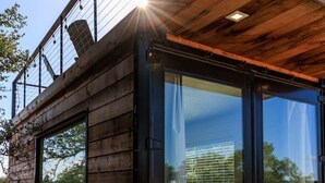 Una cabaña moderna de madera con grandes puertas de vidrio, una terraza de madera y estructura de techo metálica.