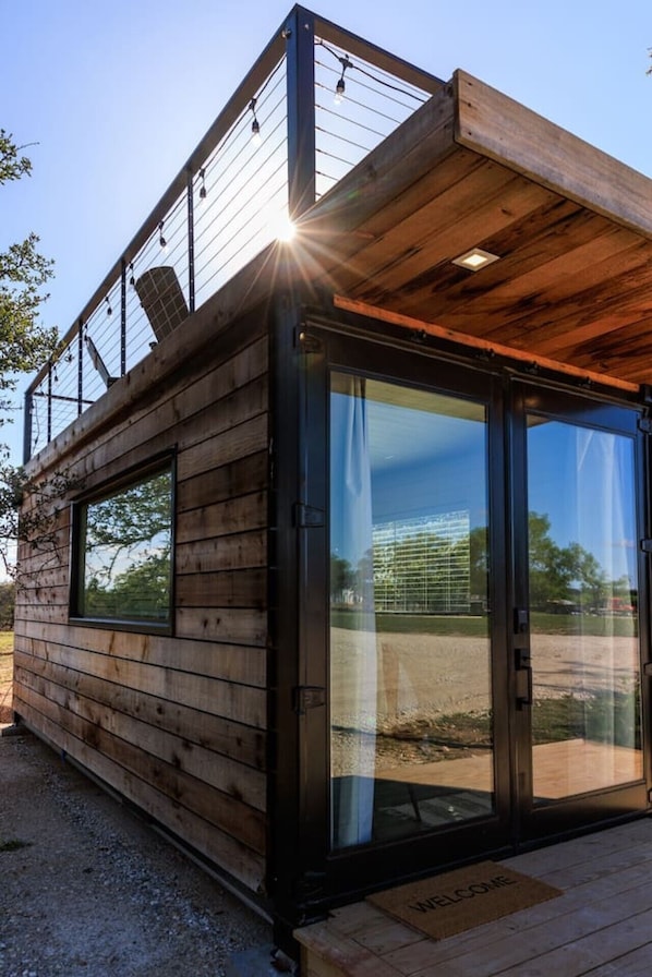 Una cabaña moderna de madera con grandes puertas de vidrio, una terraza de madera y estructura de techo metálica.