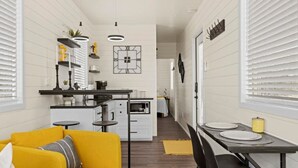 Eine kleine Küche mit weißen Schränken, ein Essbereich mit Tisch und Stühlen sowie ein gelbes Sofa.
