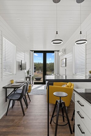 A modern kitchen with a dining area, large windows, and a view of the outdoors. - New! The Yellow Beacon-Luxury Shipping Container (Fredericksburg)