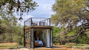 A small wooden cabin with a balcony, a bed, and a view of the surrounding trees. - Container home | Roof Patio | Countryside Views (Fredericksburg)
