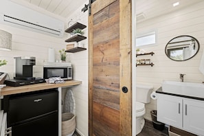 A modern kitchen with a coffee maker, microwave, and wooden shelves.