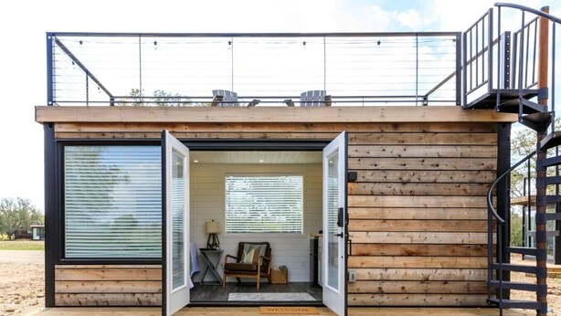 A modern cabin with a wooden exterior, a balcony, and a spiral staircase. - New! The Sunset Luxury Container Home (Fredericksburg)