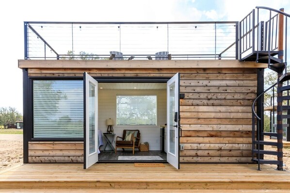 A modern cabin with a wooden exterior, a balcony, and a spiral staircase. - New! The Sunset Luxury Container Home (Fredericksburg)