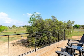 A deck with outdoor seating, a metal railing, and a view of a grassy field with trees.