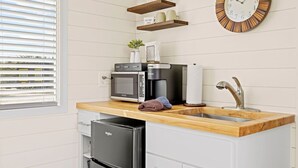 A kitchen with a microwave, coffee maker, sink, and a clock on the wall. - New! The Sunset Luxury Container Home (Fredericksburg)