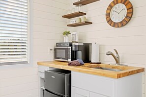 A kitchen with a microwave, coffee maker, sink, and a clock on the wall. - New! The Sunset Luxury Container Home (Fredericksburg)