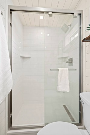 Un bagno moderno con doccia vetrata, piastrelle bianche e vaso sospeso bianco.