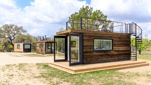 A modern cabin with a glass door entrance, a wooden deck, and a spiral staircase. - New! The Perry-Chic container home Oasis (Fredericksburg)