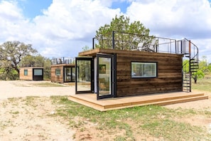 Une cabane moderne avec une entrée dotée d’une porte en verre, une terrasse en bois et un escalier en colimaçon.