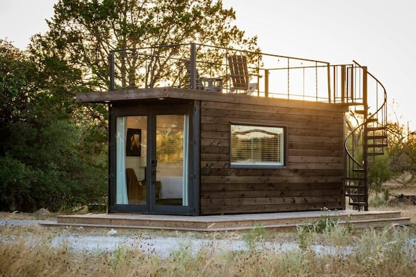 Una cabaña pequeña con una puerta de cristal, una ventana y una escalera de caracol.