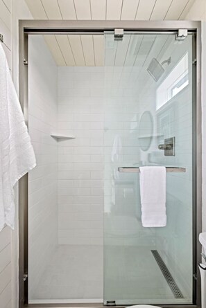 A glass-enclosed shower stall with a white towel on the wall, a glass door, and a visible drain.