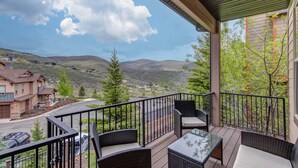 Ein Balkon mit Korbmöbeln, einem Glastisch und Blick auf eine hügelige Landschaft.
