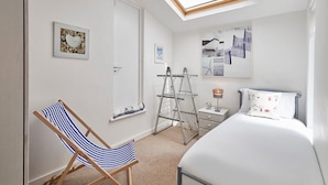 Une chambre à coucher avec un lit, une chaise, une échelle, une étagère et des œuvres d’art accrochées aux murs.