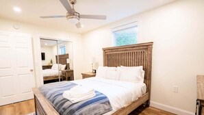 Ein Schlafzimmer mit einem Holzbett, Deckenventilator, Fenster und Spiegel.