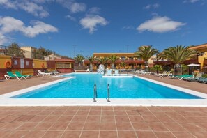 Una piscina con tumbonas y palmeras, rodeada de edificios con fachadas rojas y amarillas.