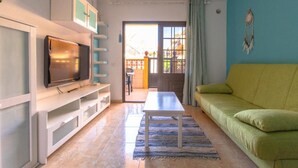 Un salón con televisor, sofá, mesa de centro y vista al exterior.