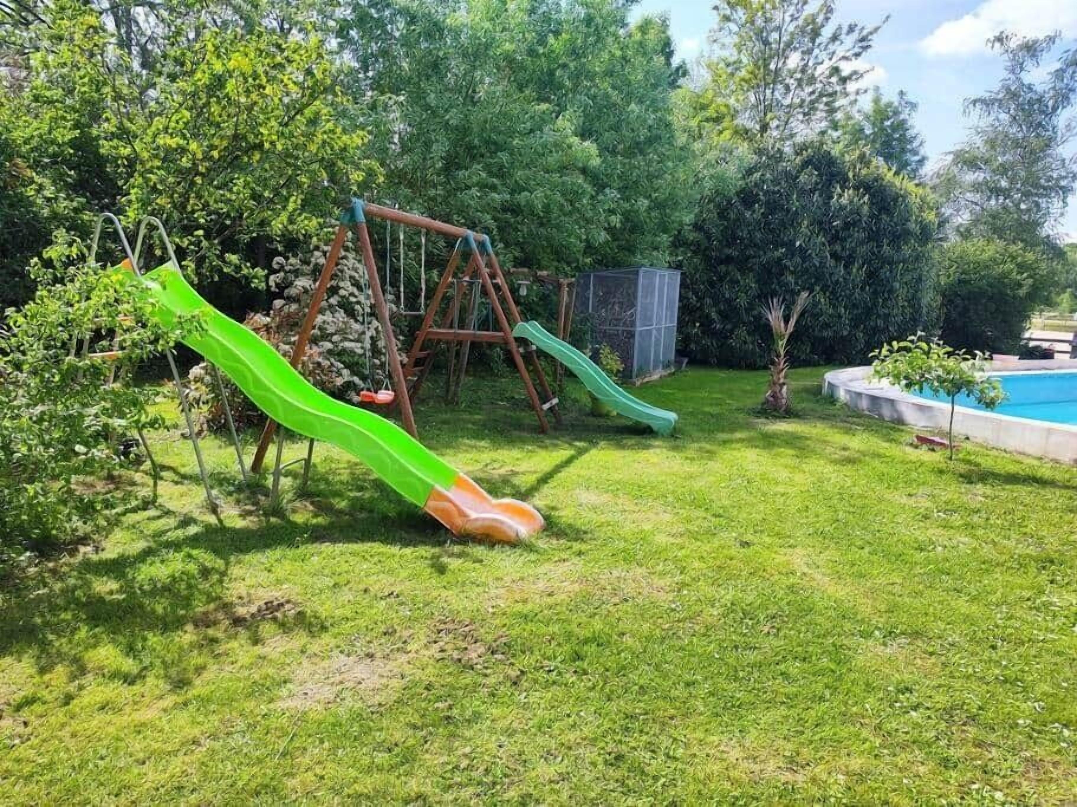 Un patio trasero con un columpio, un tobogán, un árbol pequeño y una piscina.