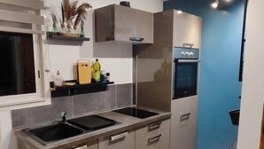 A modern kitchen with stainless steel appliances, a built-in oven, and a window with blinds. - Gîte du Moulin de Tart le Bas (Tart-le-Bas)