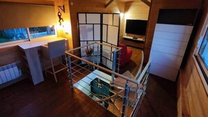 A compact room with a wooden interior, a small desk with a chair, a TV mounted on the wall, and a glass railing overlooking a lower level. - Gîte du Moulin de Tart le Bas (Tart-le-Bas)