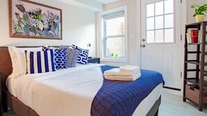 A bedroom with a bed, pillows, a painting, a window, and a bookshelf. - Lux CoHi Cove - Walk to METRO Sub Shopping & More (Washington DC)