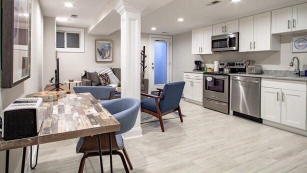 A modern kitchen with white cabinets, stainless steel appliances, and a dining area with a wooden table and blue chairs. - Lux CoHi Cove - Walk to METRO Sub Shopping & More (Washington DC)