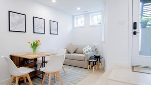 Una sala de estar moderna con un sofá, una mesa de centro y un comedor con sillas y una mesa. Hay mapas enmarcados en la pared y un jarrón con flores sobre la mesa de centro.
