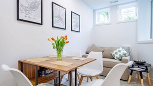 Una sala de estar moderna con una mesa de comedor de madera, sillas blancas, un sofá beige y cuadros con vistas de la ciudad en la pared.