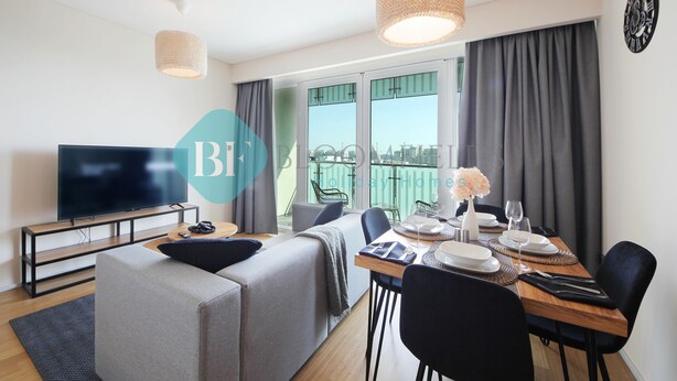 Ein modernes Wohnzimmer mit Flachbildfernseher, einer Couch, einem Esstisch für zwei Personen und einem Balkon mit Aussicht.