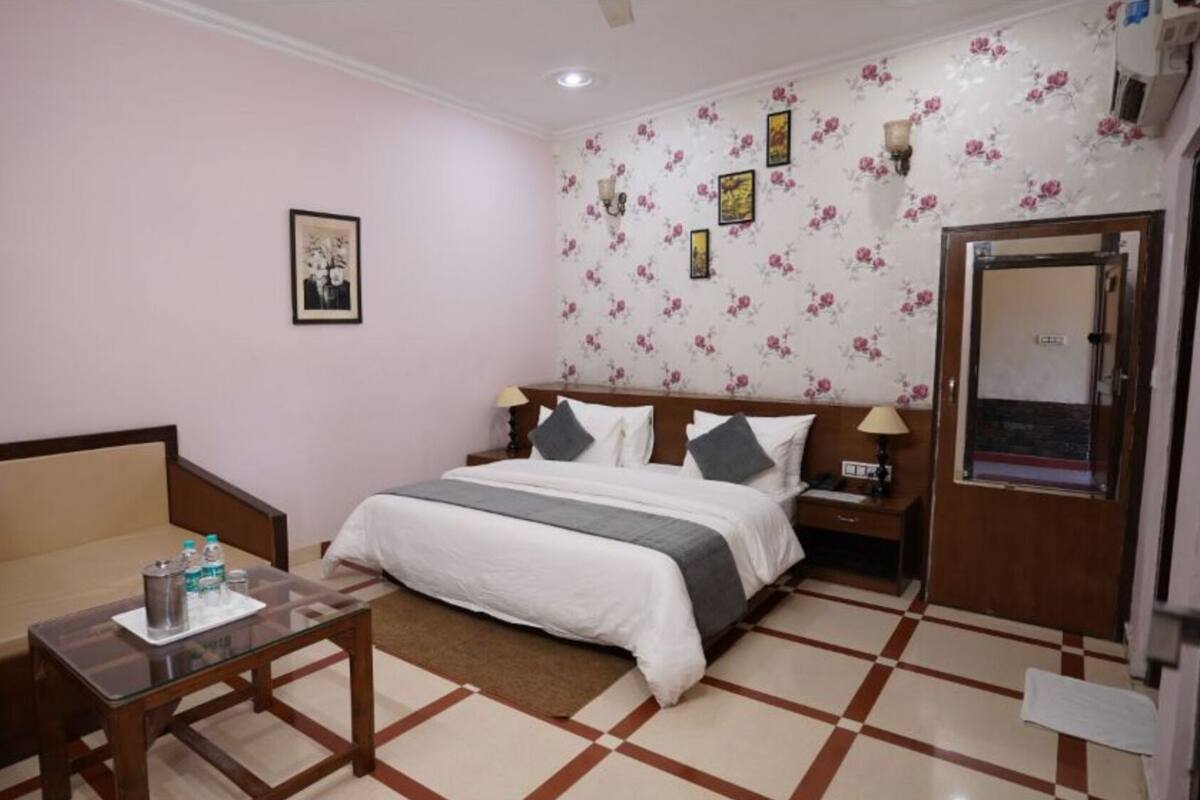 A hotel room with a bed, a sofa, a small table with water bottles, a nightstand, and a door.