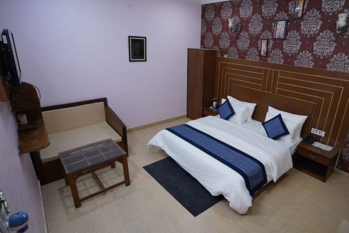 A hotel room with a bed, bedside tables, a chair, a small table, and a patterned wall.