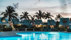 Een zwembad met ligbedden, palmbomen en een resort-achtig gebouw in de schemering.