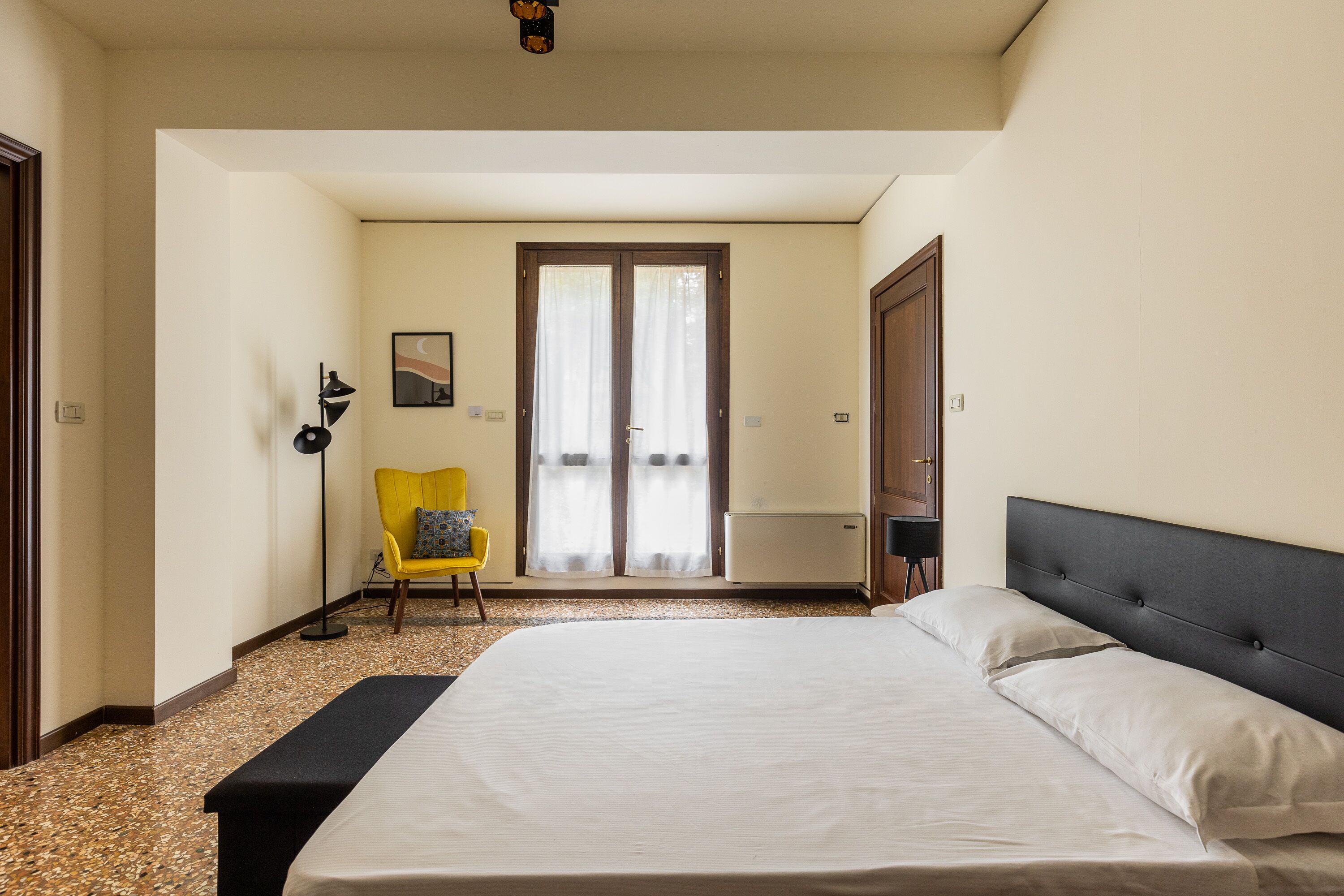 Habitación de hotel con una cama, una silla, un escritorio y una puerta que da a un balcón.