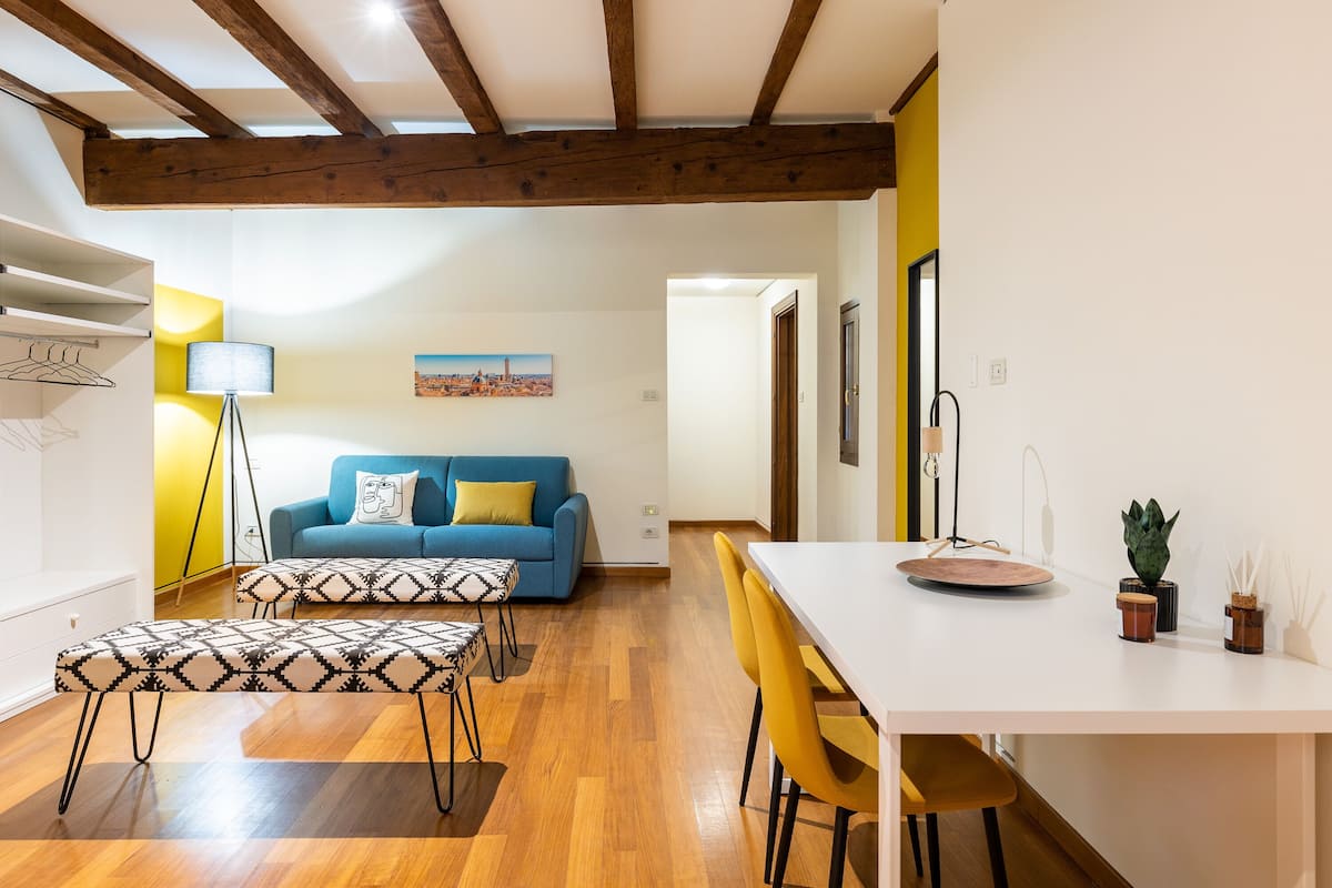 Una sala moderna con un sofá azul, un otomano estampado y sillas amarillas.