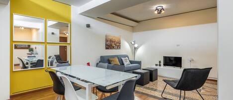 Una sala de estar moderna con una mesa de comedor de vidrio, sillas blancas y negras, un sofá y un televisor.