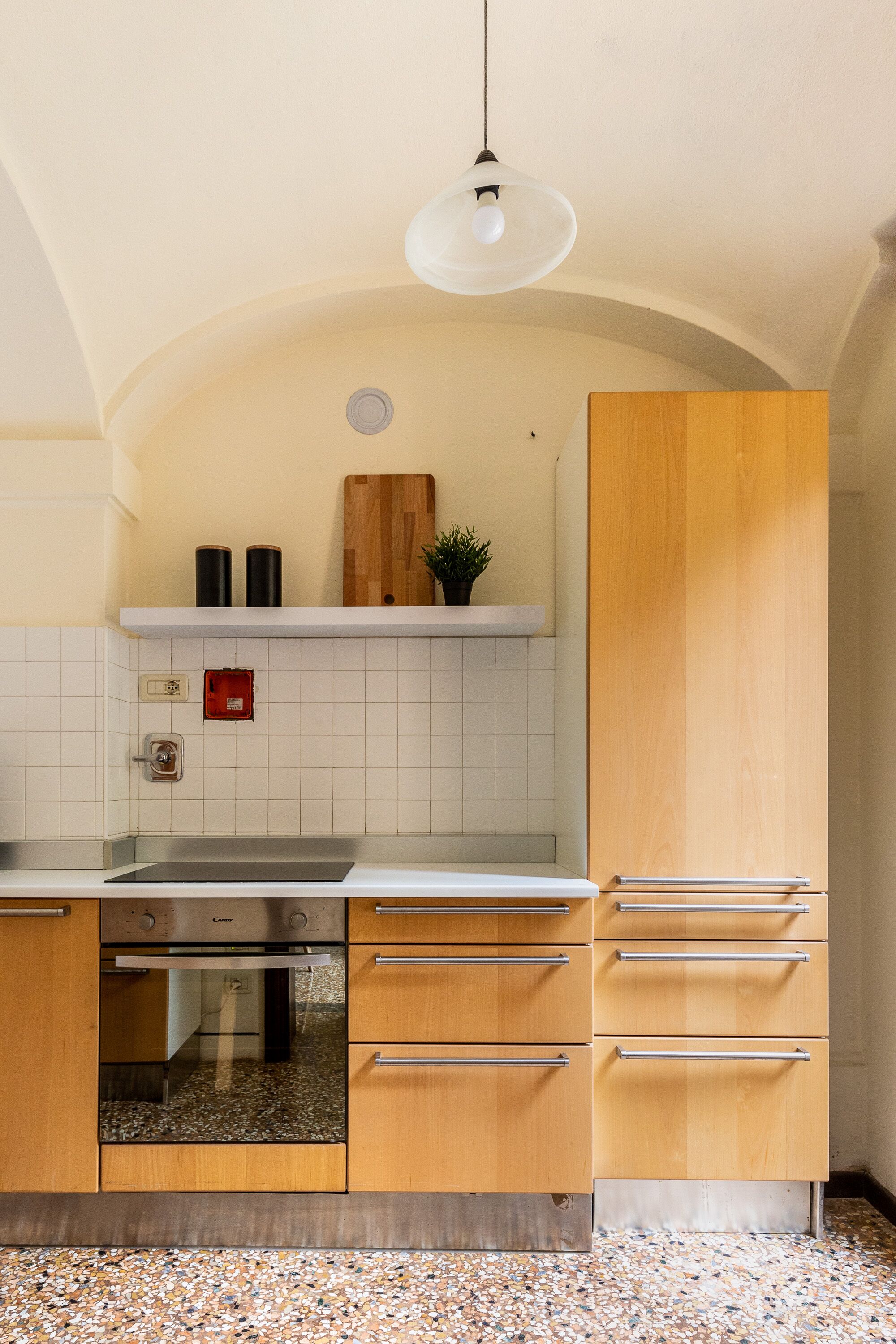 Una cocina con paredes de azulejos blancos, un armario de madera, un horno de acero inoxidable y una encimera de granito.