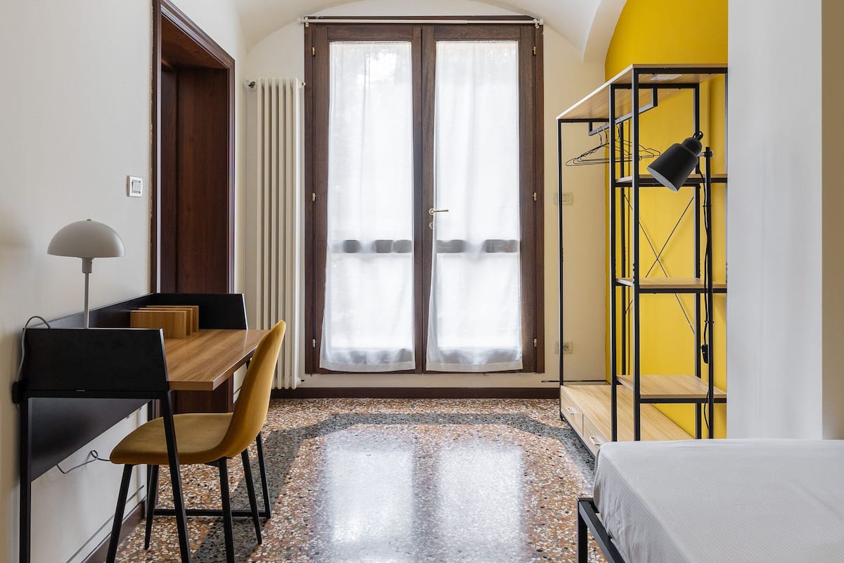 Una habitación con cama, escritorio, silla y estantería amarilla.