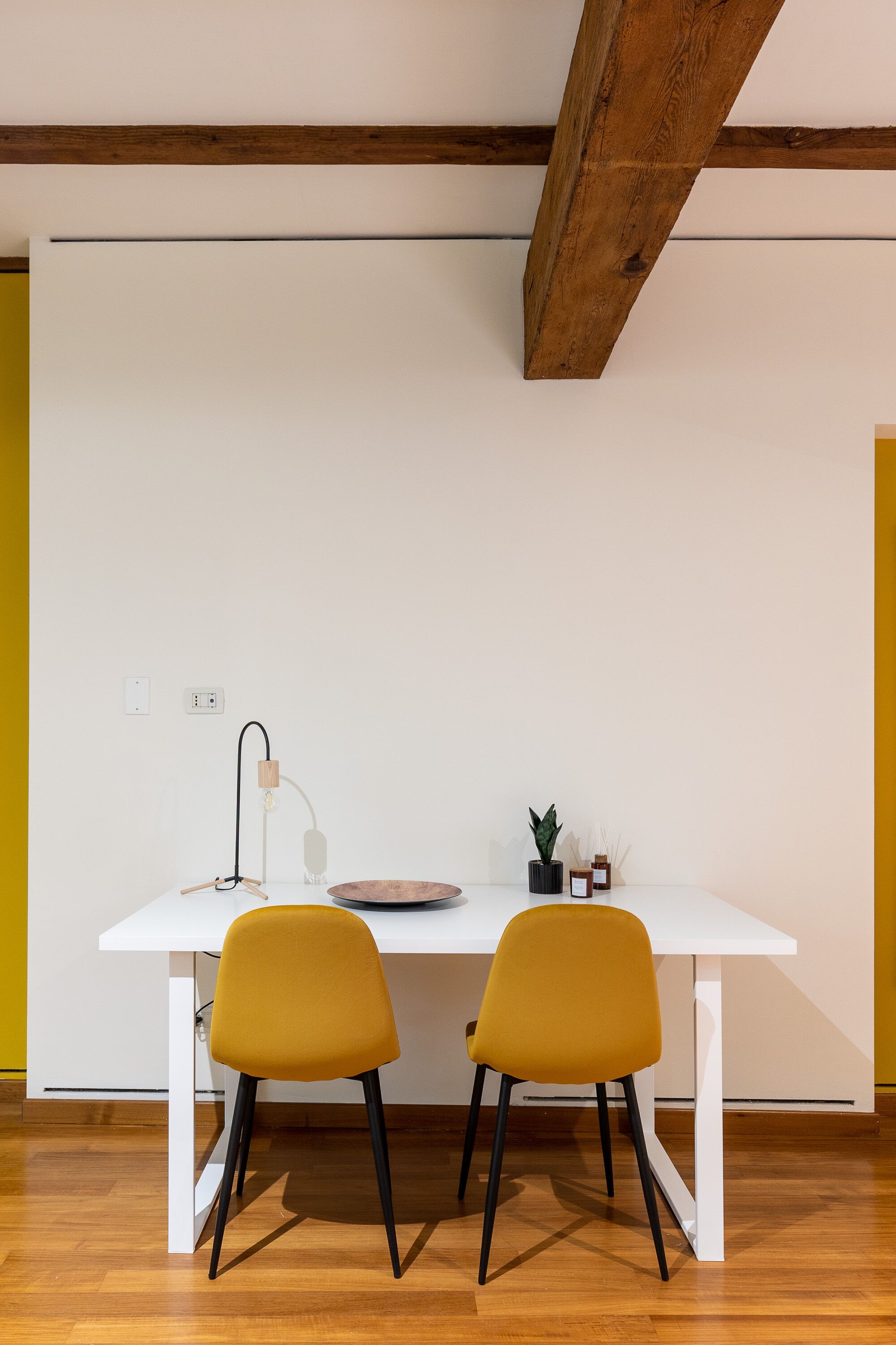 A white table with two mustard chairs, a lamp, and a small plant on the table.