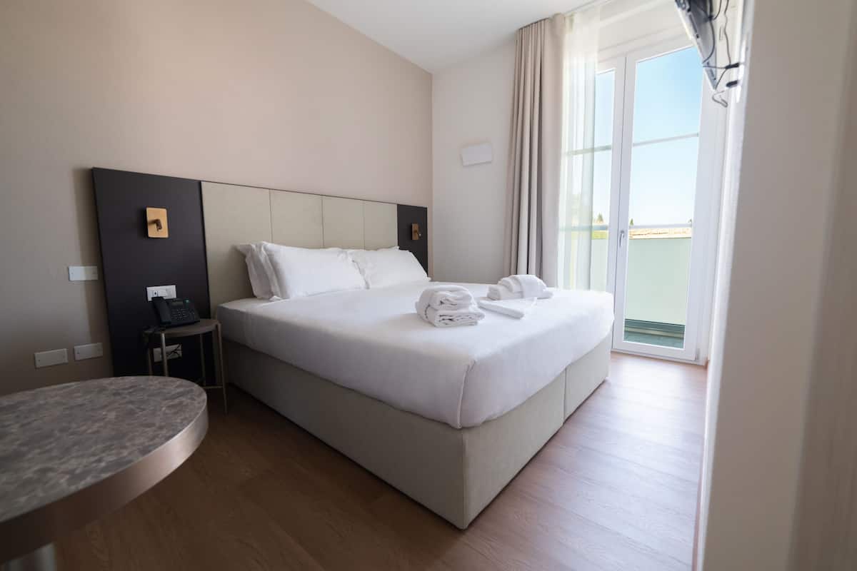 A hotel room with a large bed, a bedside table, a phone, and a view of the outdoors.