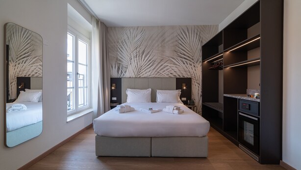 Una habitación de hotel moderna con una cama grande, un armario empotrado, una zona de cocina y un espejo amplio.
