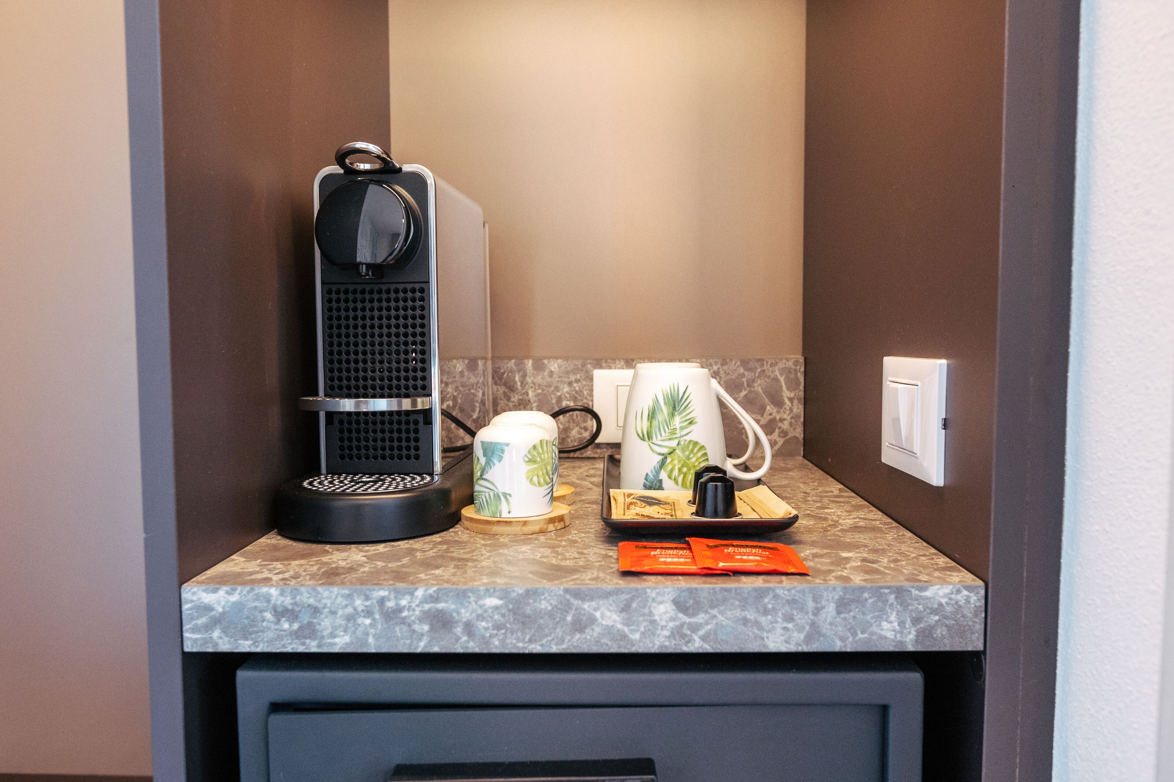 A compact kitchenette with a coffee maker, a kettle, and a tray with a cup and a small orange item.
