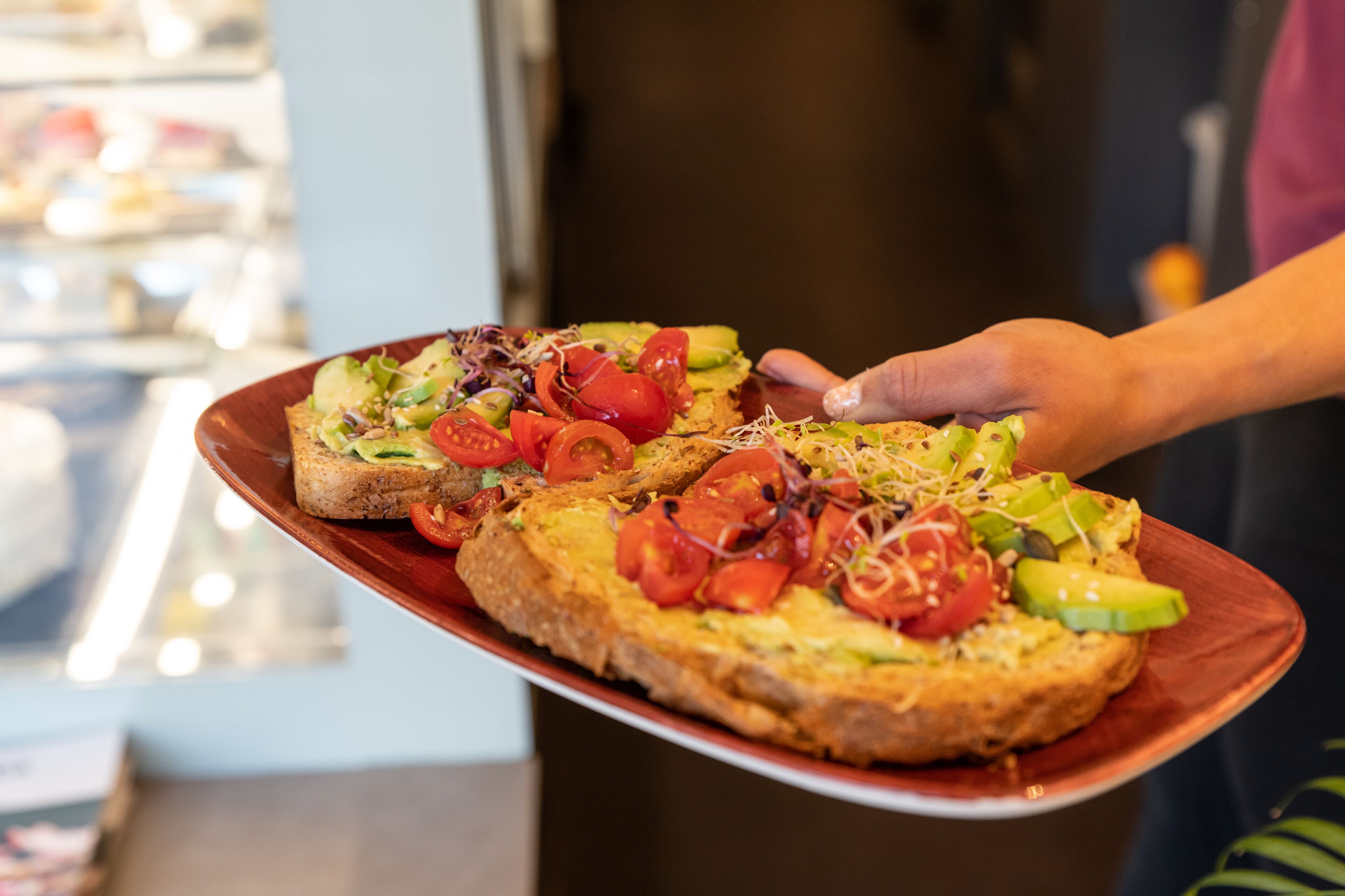A person holding a plate with two pieces of toast topped with vegetables.