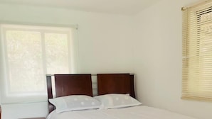 Une chambre à coucher avec un grand lit, une table de chevet, une fenêtre avec des stores et un plancher carrelé.