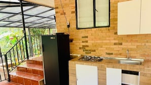 Une cuisine compacte équipée d’une cuisinière à gaz, d’un évier et d’un réfrigérateur. Des marches mènent à un espace extérieur abrité, agrémenté d’une rambarde en métal.