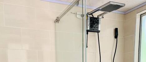 A glass-enclosed shower with a handheld showerhead, a glass door, and a tiled floor.