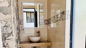 Une salle de bain avec un mur en pierre, un lavabo blanc et un miroir.