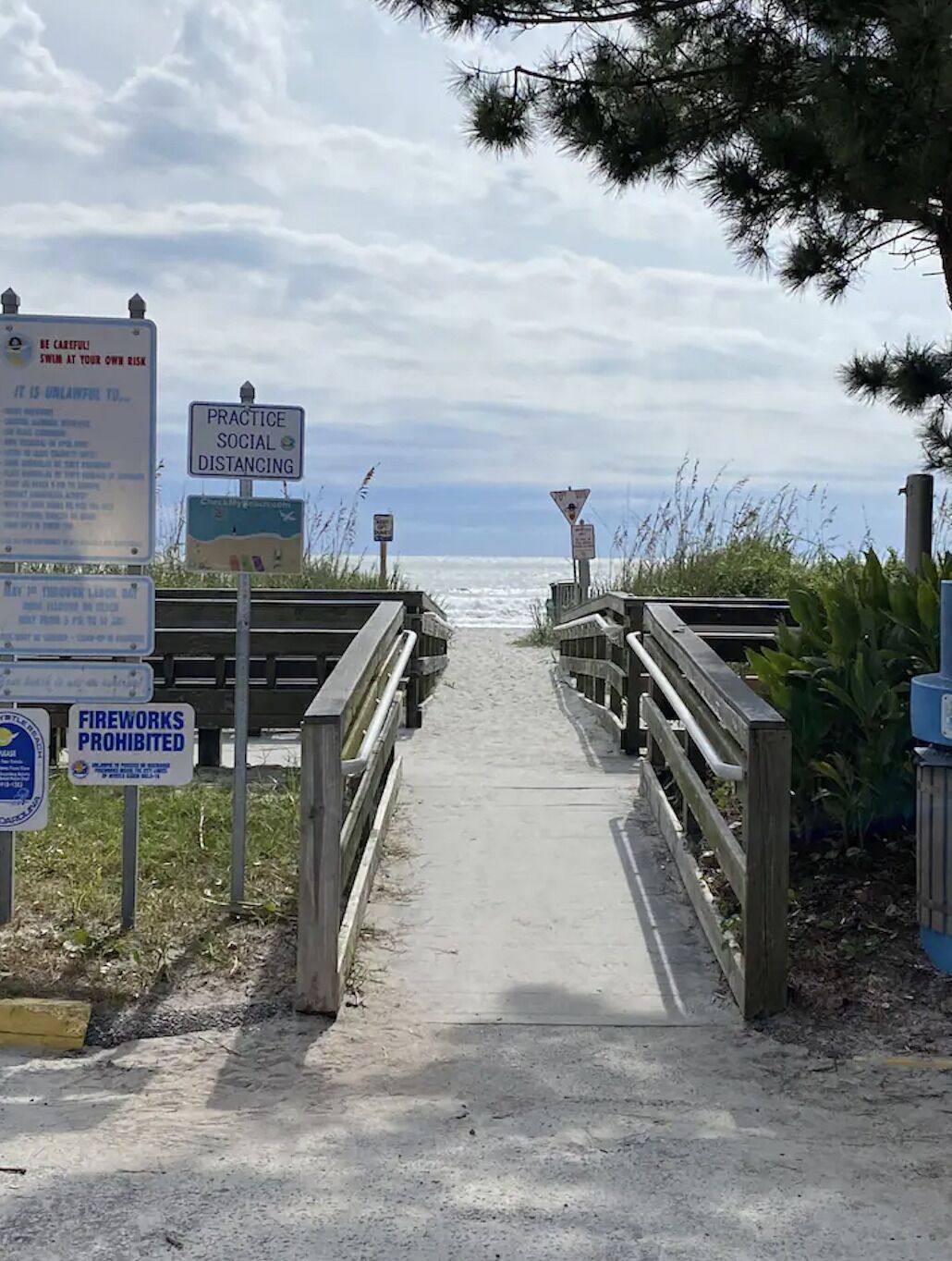 A pathway leading to a beach with signs about social distancing and fireworks prohibition.